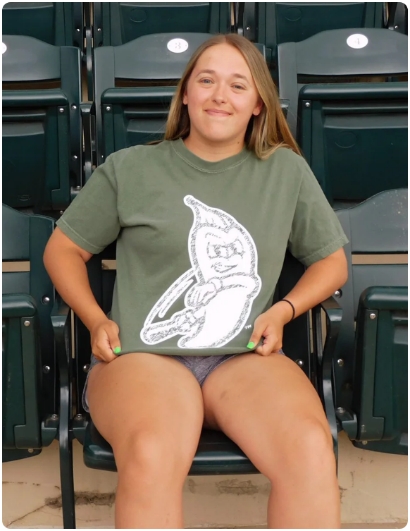 Model sitting in stadium seating wearing an olive green Tri-City Chili Peppers t-shirt with a white outlined mascot logo